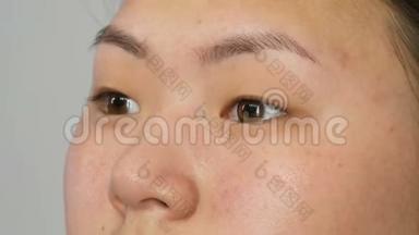 一位专业的化妆师将带有特殊画笔的遮瑕膏应用于视觉工作室特写的亚洲女孩模特脸上